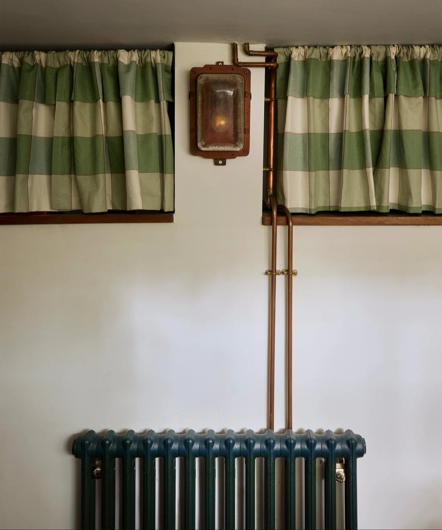 Green and white striped curtains on a warm white wall with a radiator below.