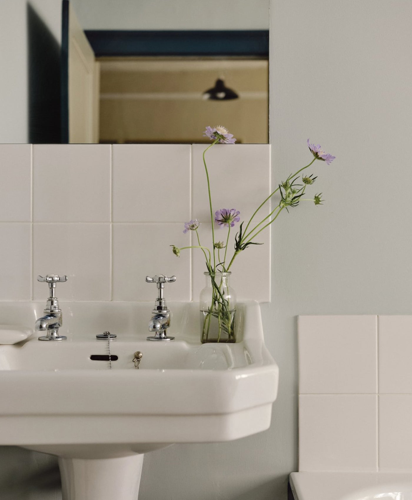 Bathroom sink with a vase of flowers on a tiled wall with blue grey paint