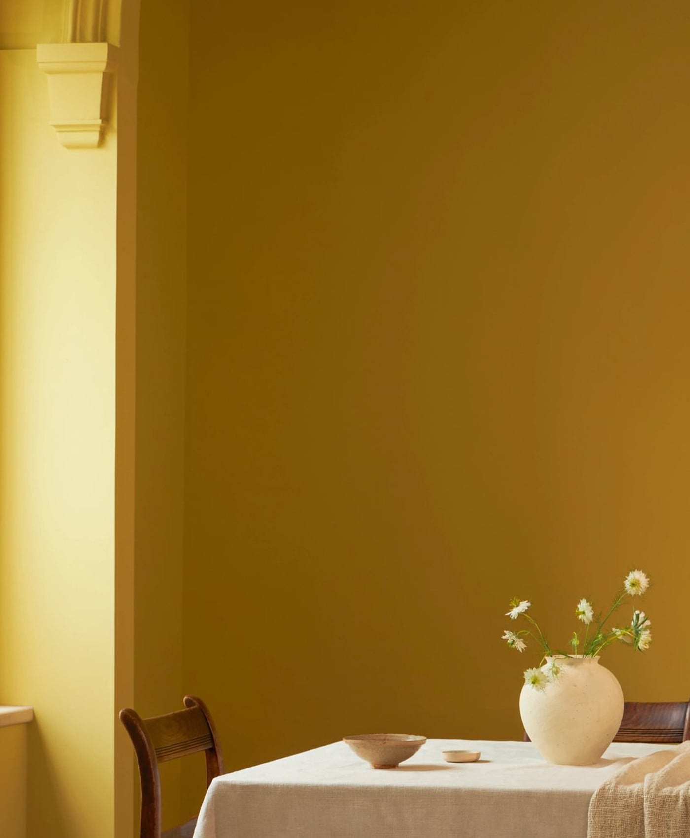 Dining room with a yellow wall, table, chairs, and a vase with flowers.