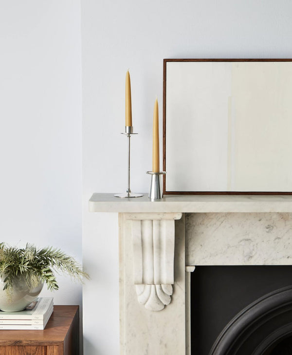 Decorative setup on a fireplace mantle with candles and a framed picture walls painted in cool white paint