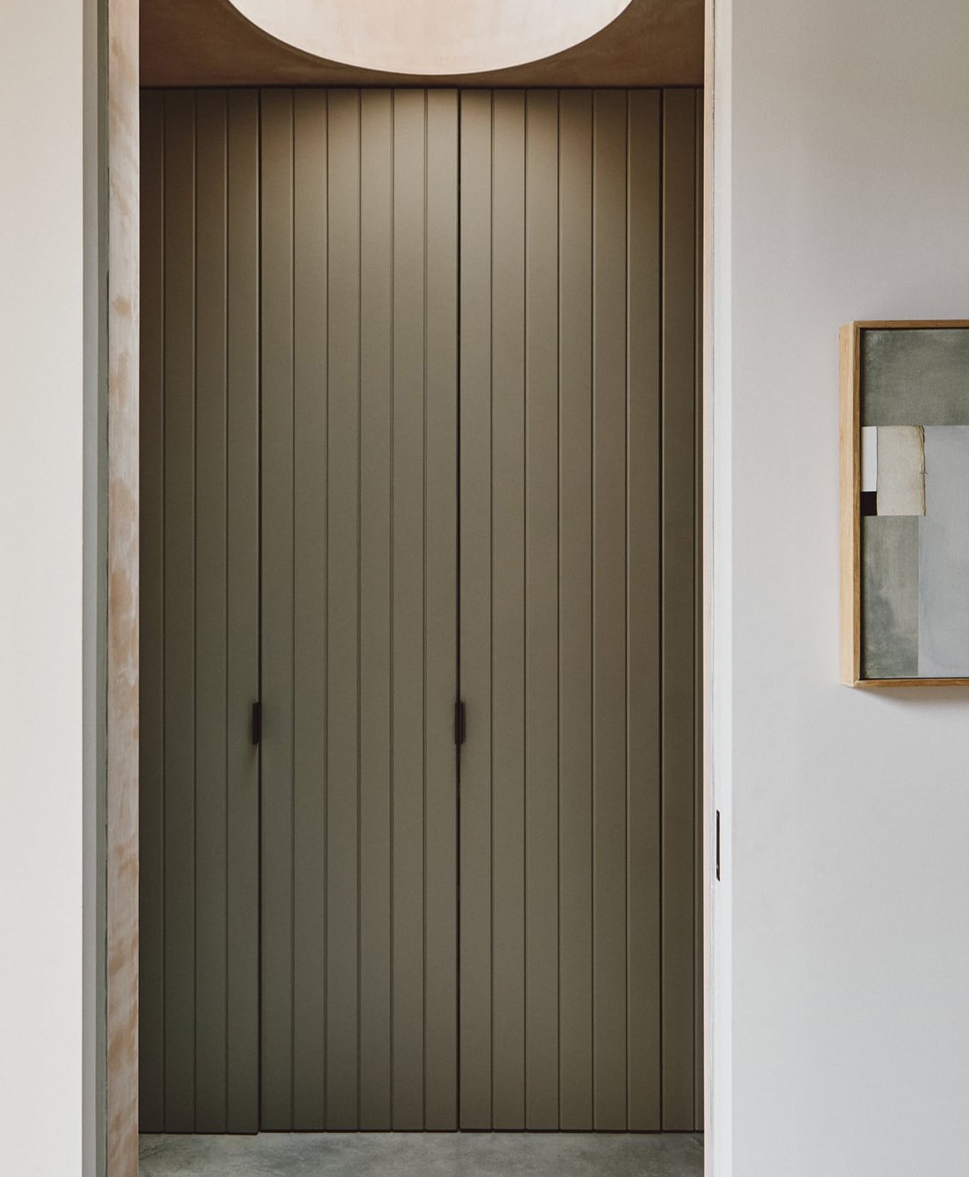 Modern interior with a closed wooden door painted in a sage green paint and a minimalistic wall decoration.