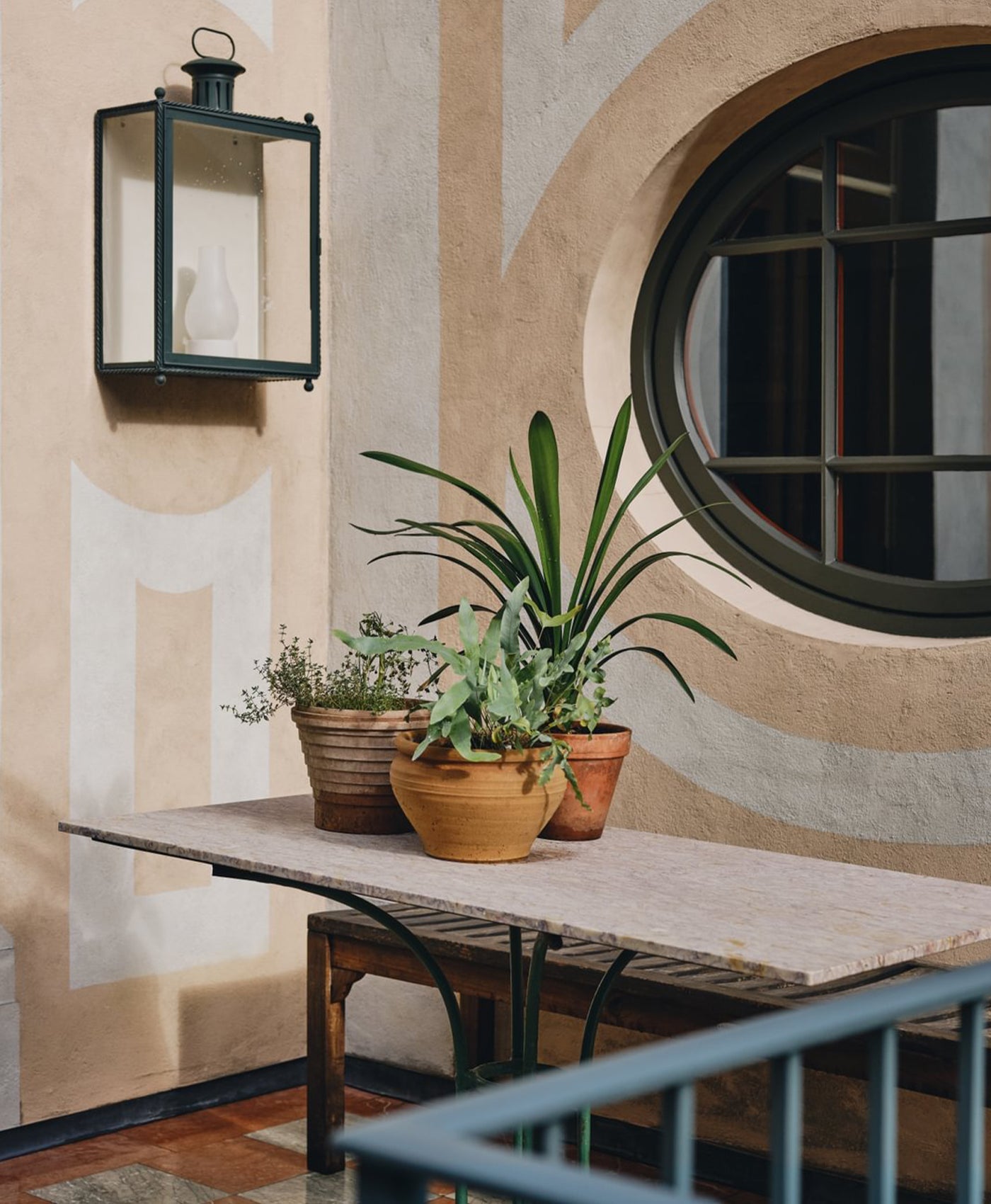 Decorative wall with a lantern, round window, and potted plants on a table.