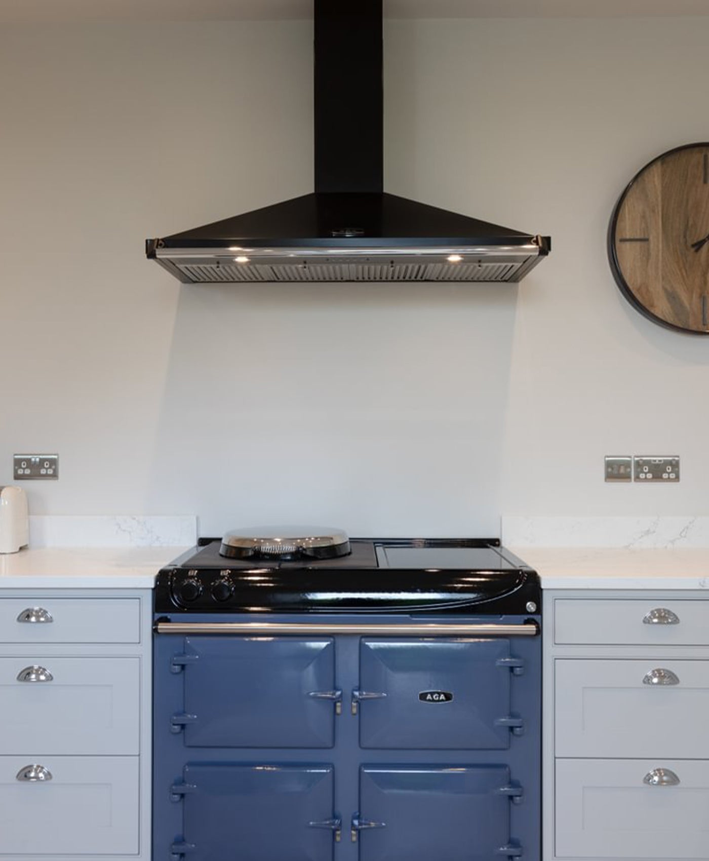 Blue Aga stove in a kitchen with a black range hood and white walls.