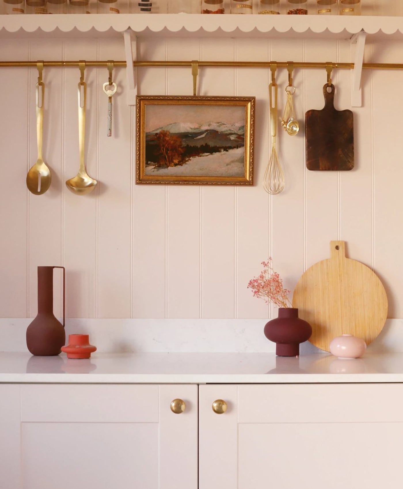 Kitchen interior with utensils, vases, and a painting on a light pink wall.
