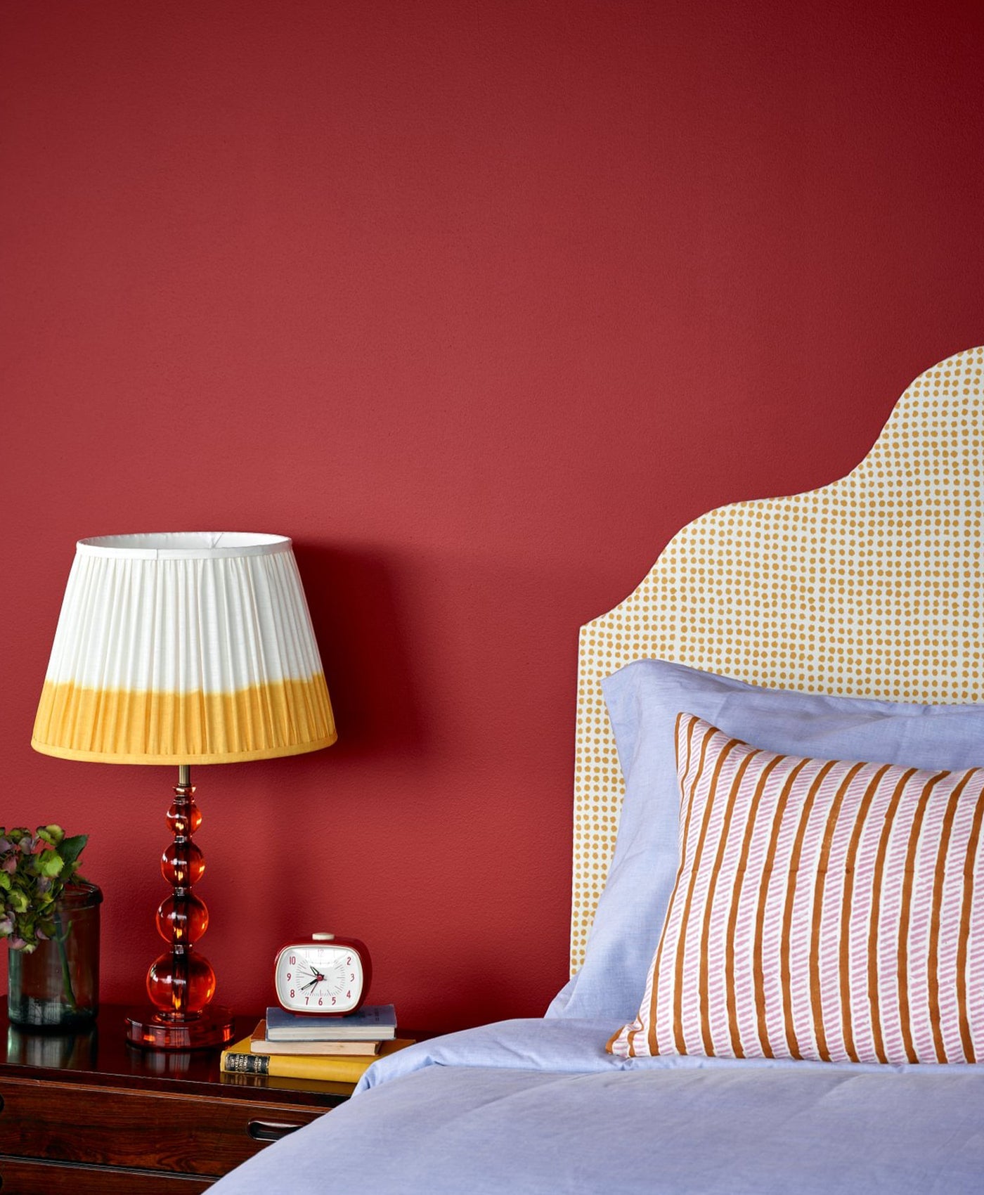 Bedroom in deep red paint, lamp, and bed with striped pillows.