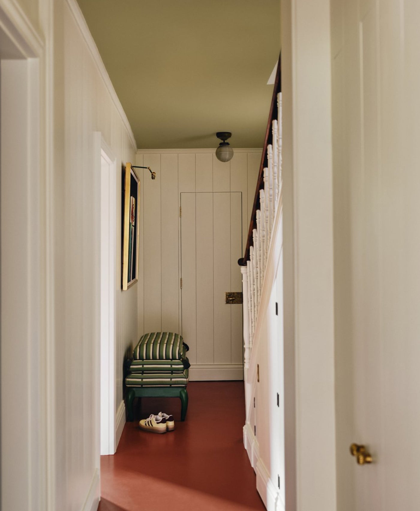 Foyer with a staircase in off-white, floor in terracotta red, and ceiling in a light olive paint.