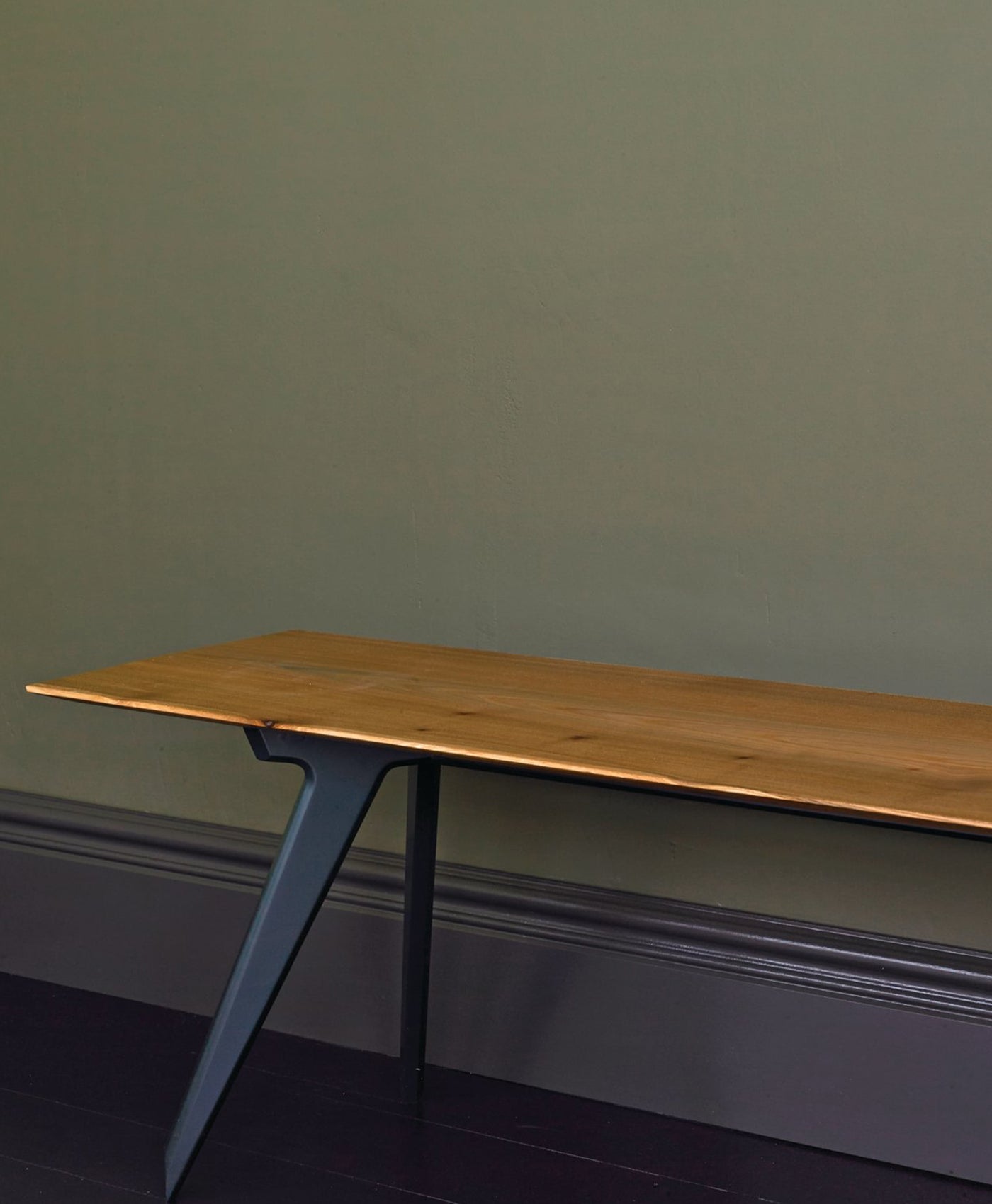 Wooden desk with metal legs against a dark olive green wall