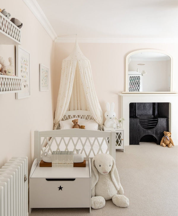 Pale pink nursery room with a crib, teddy bear, and decorative elements.