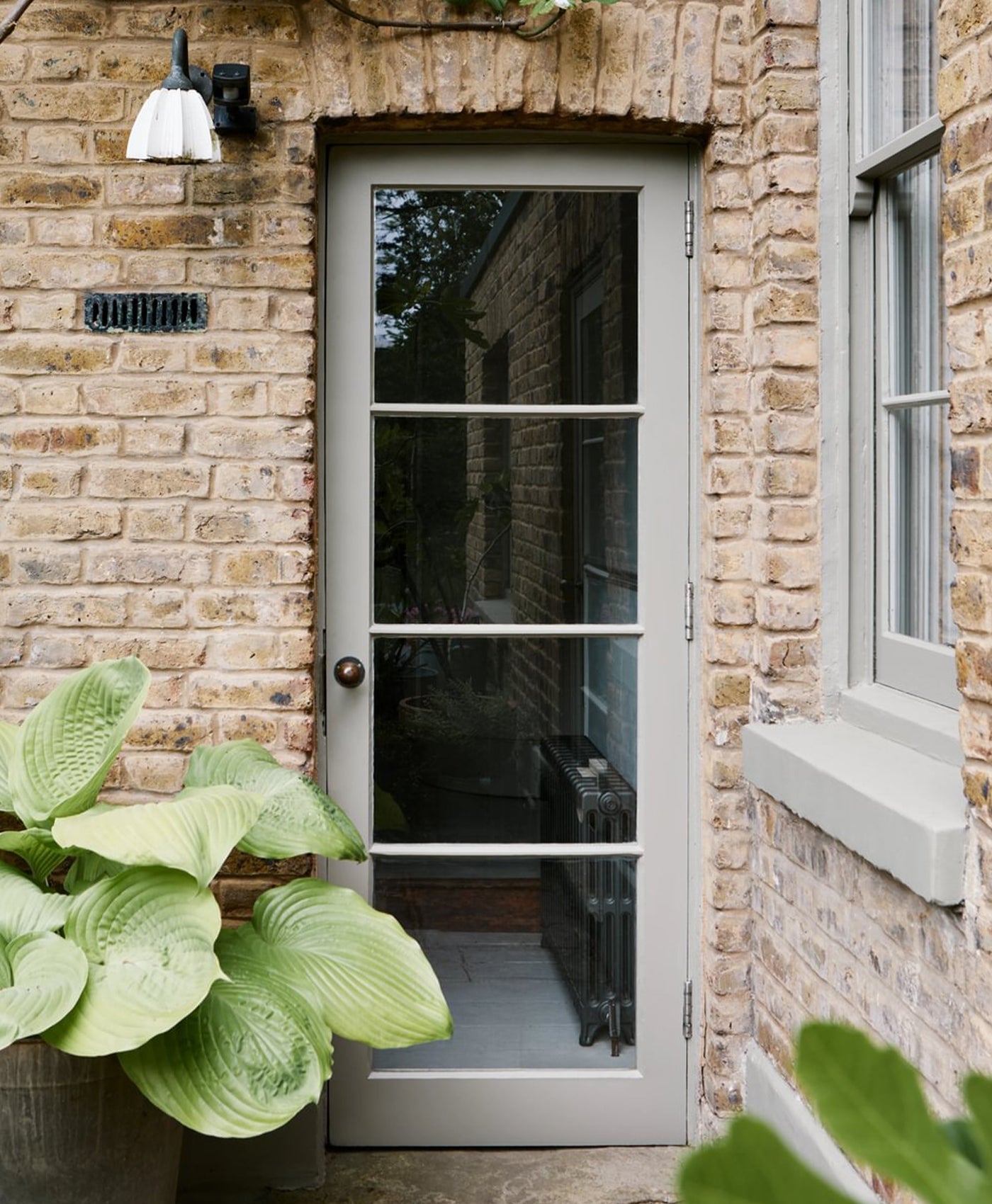 Sage green door on a brick wall with plants in the foreground