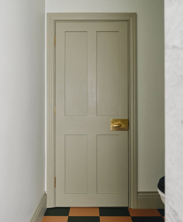 Sage green door with a gold handle on a light green wall with a checkered floor.