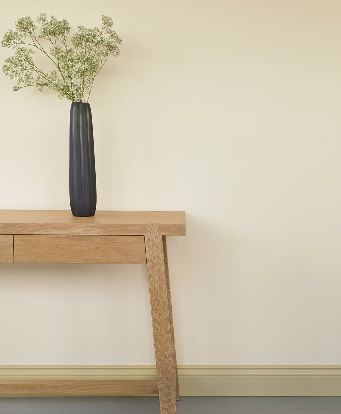 Black vase with greenery on a wooden table against a beige wall