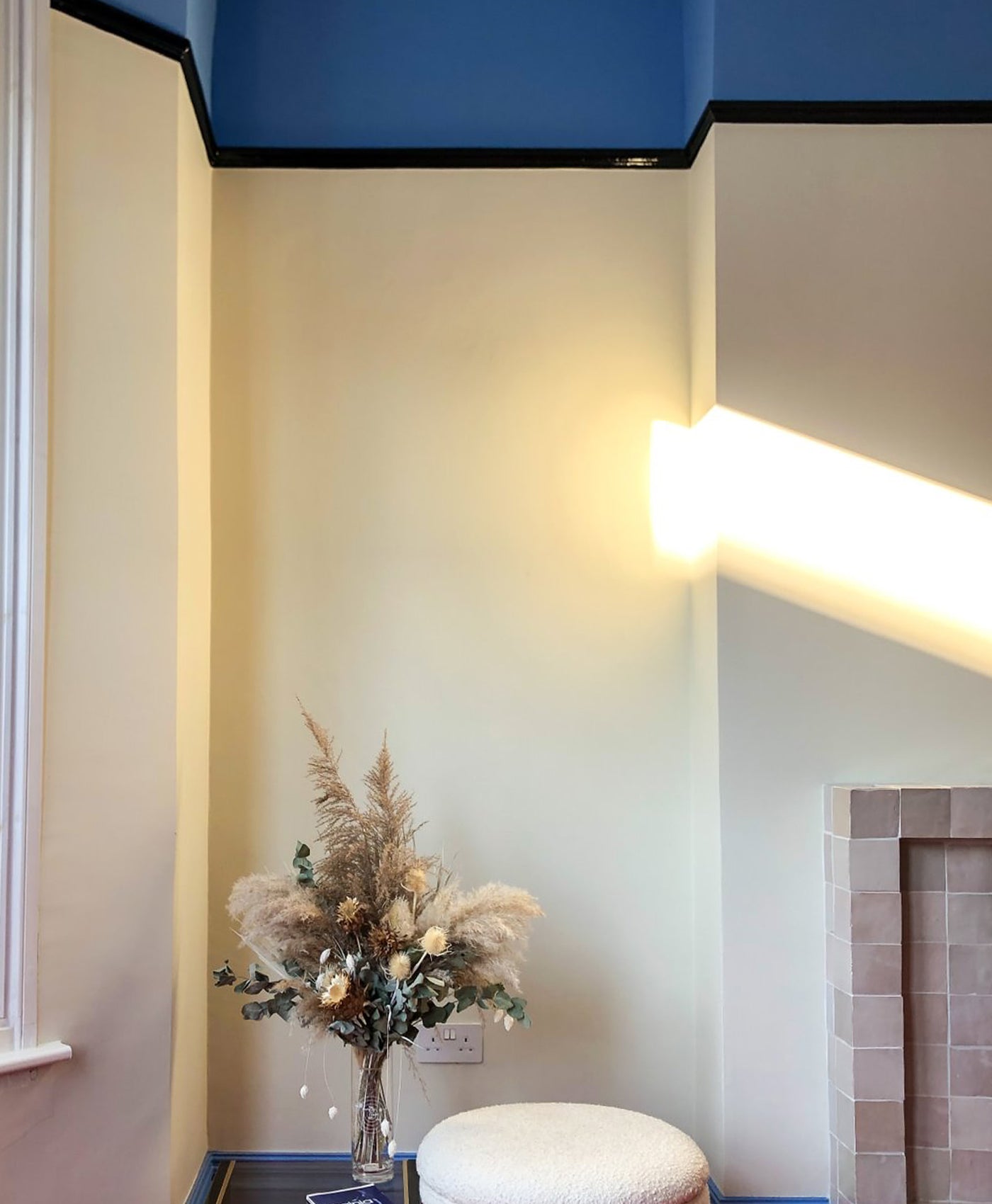 Decorative plant in a vase on a small table against a wall with a light fixture.