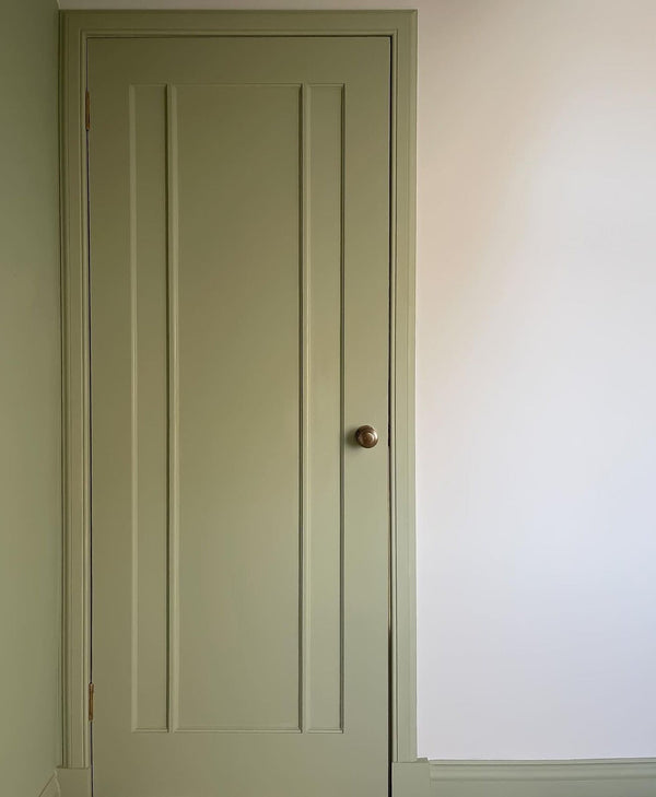 Green door with a brass handle on a warm grey wall