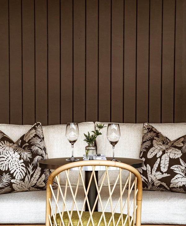 Sofa with decorative pillows and a small table with glasses against a mocha brown wooden panelled wall.