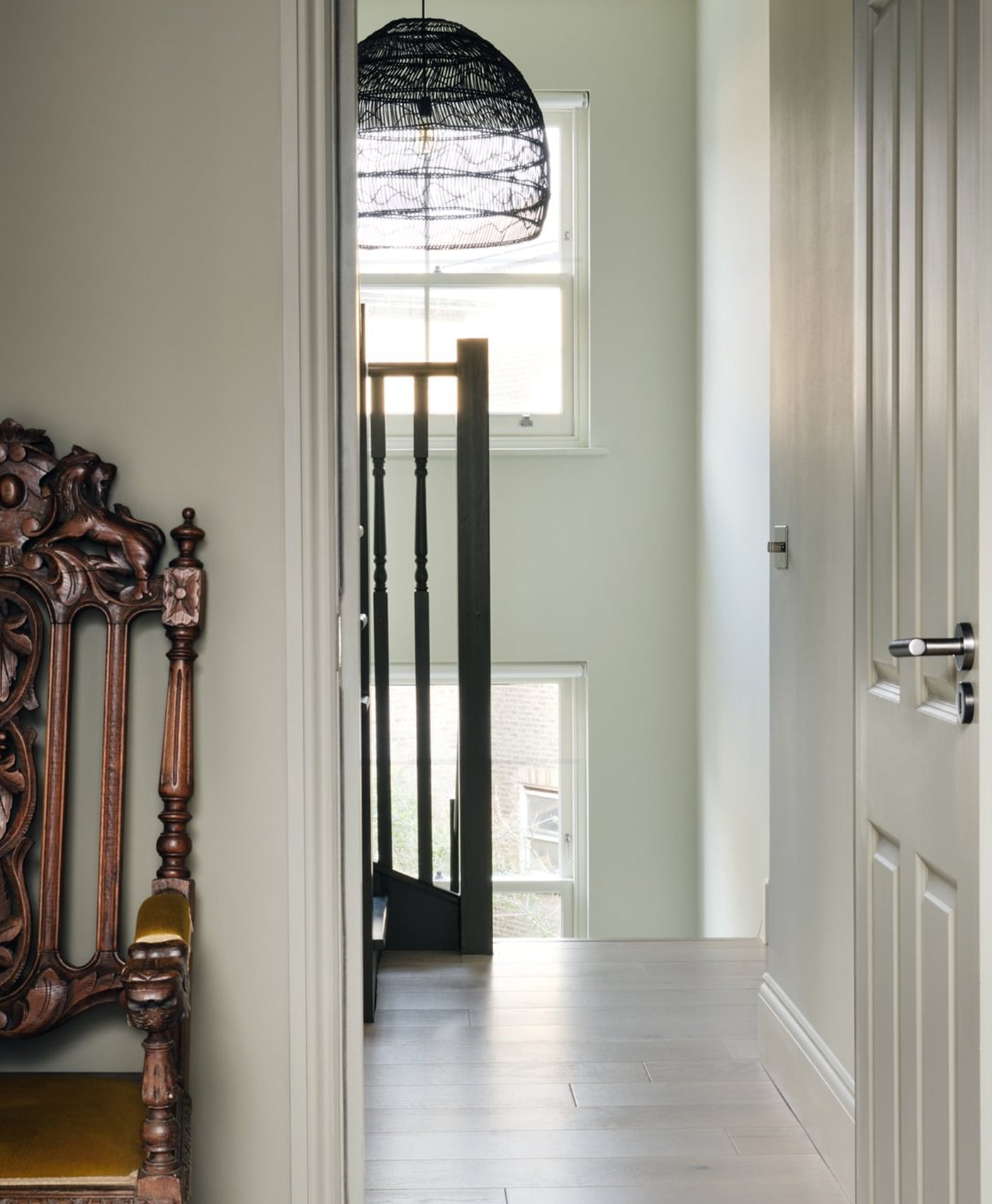 white hallway with ornate wooden chair, open door, and light green walls.
