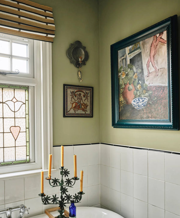 Bathroom painted olive green with a candle holder, framed artwork, and stained glass window.