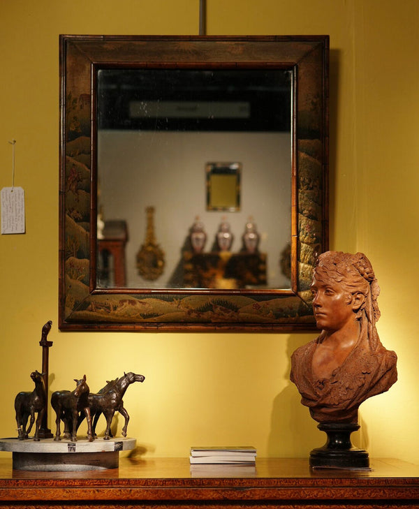 Decorative mirror with a wooden frame on a yellow wall, featuring a bust and small sculptures.