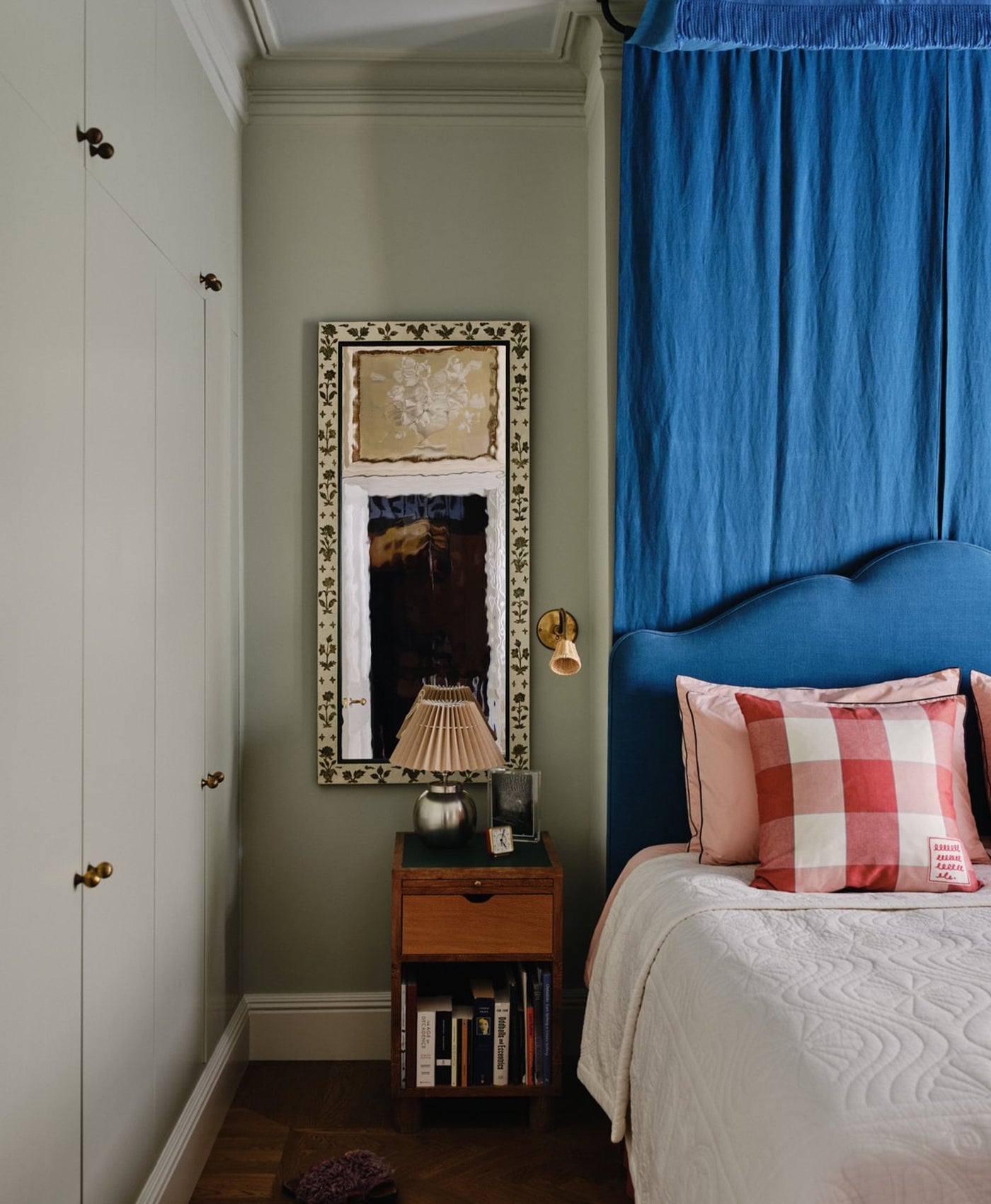 Mint green bedroom with blue headboard, plaid pillow, and decorative mirror.