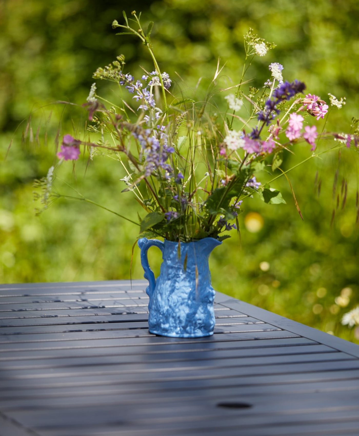 Blue ceramic vase with wildflowers on a wooden table painted in deep blue outdoors