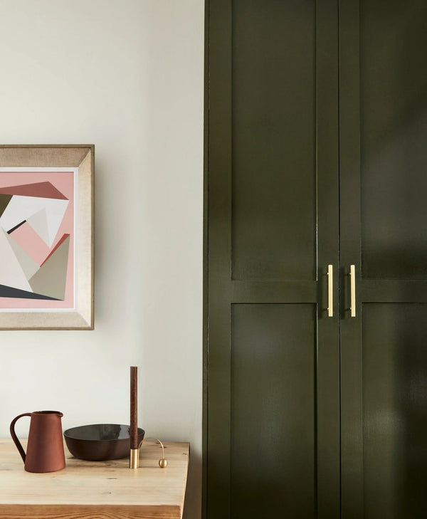 Green kitchen cabinet with gold handles next to a wall with a framed abstract art piece.