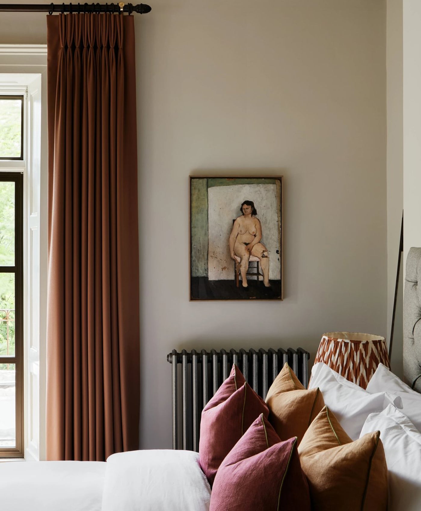 Stone white room interior with a painting on the wall, radiator, and colourful pillows.