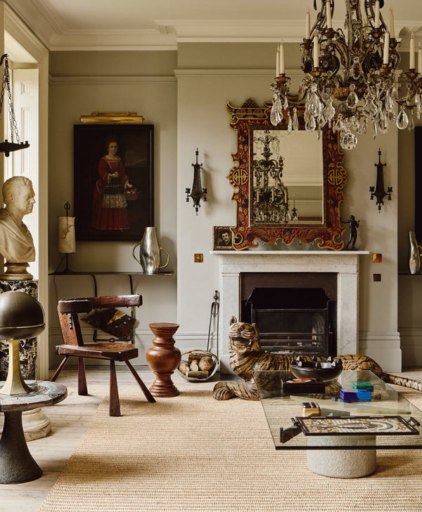 Warm grey living room with classical decor, including a chandelier, fireplace, and various sculptures.