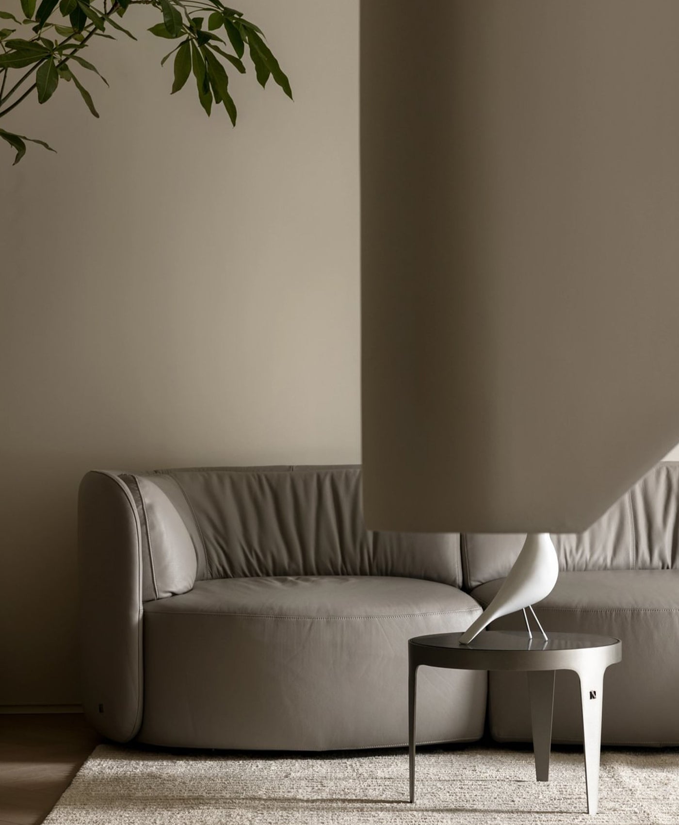 Modern grey sofa against a neutral wall with a small table and plant.