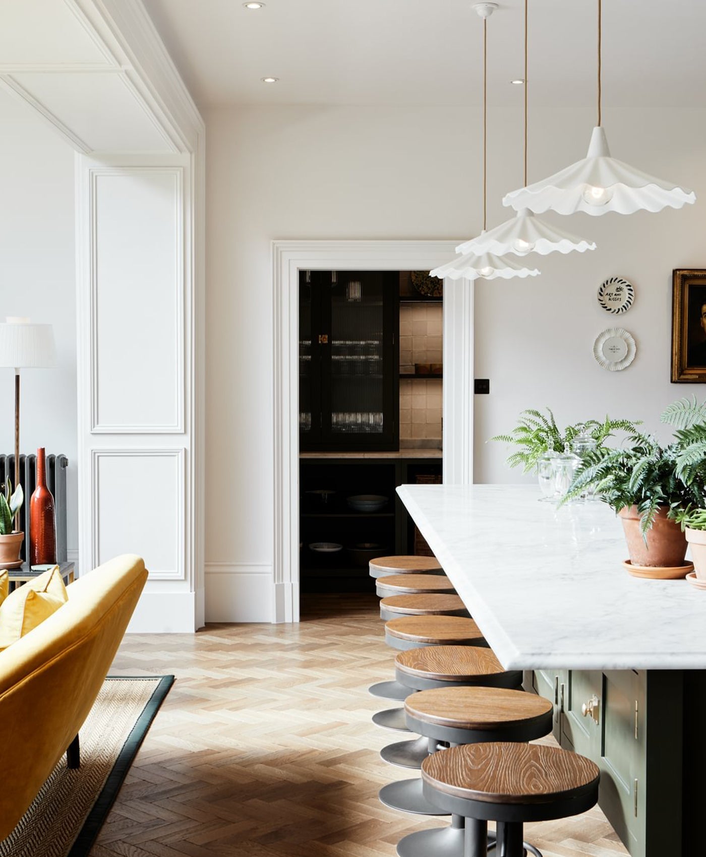 Off-white pink modern kitchen with white island, stools, and a yellow chair.