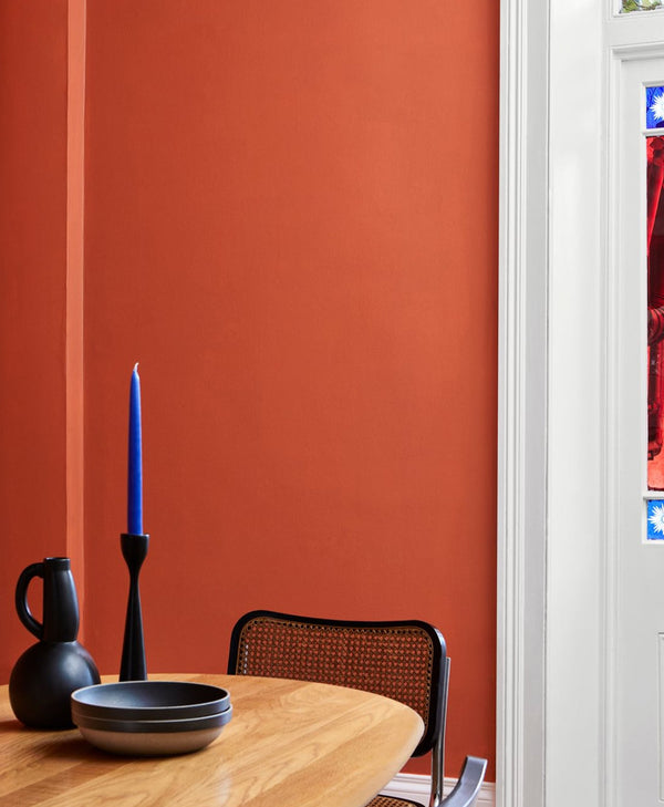 Orange dining area with a wooden table, black chairs, and a blue candle