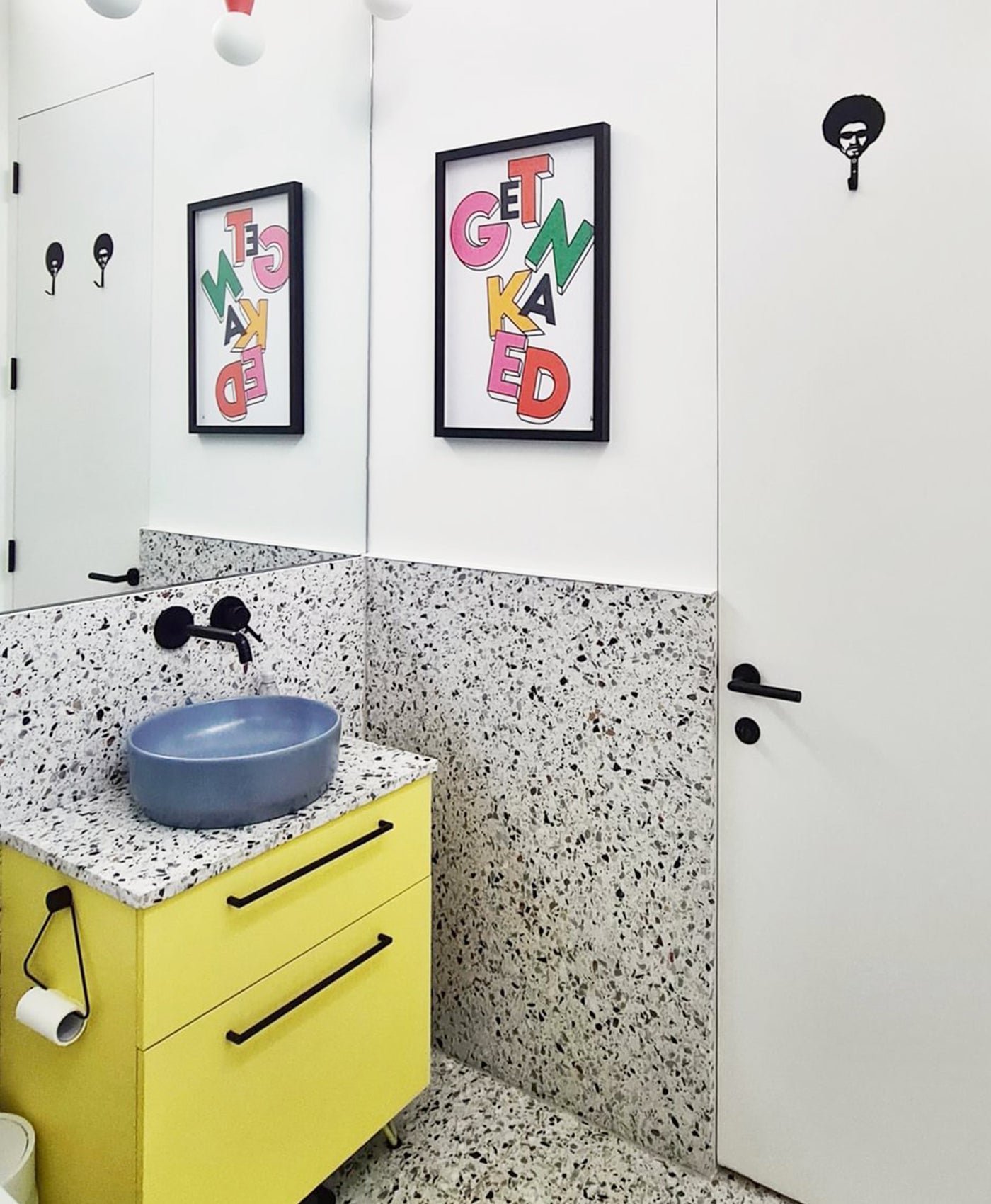 Bathroom with yellow vanity, speckled gray walls, and colorful wall art.