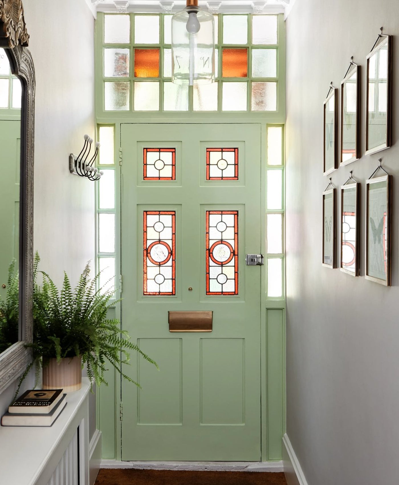 Pistachio Green front door with glass panels in a hallway with plants and mirrors.