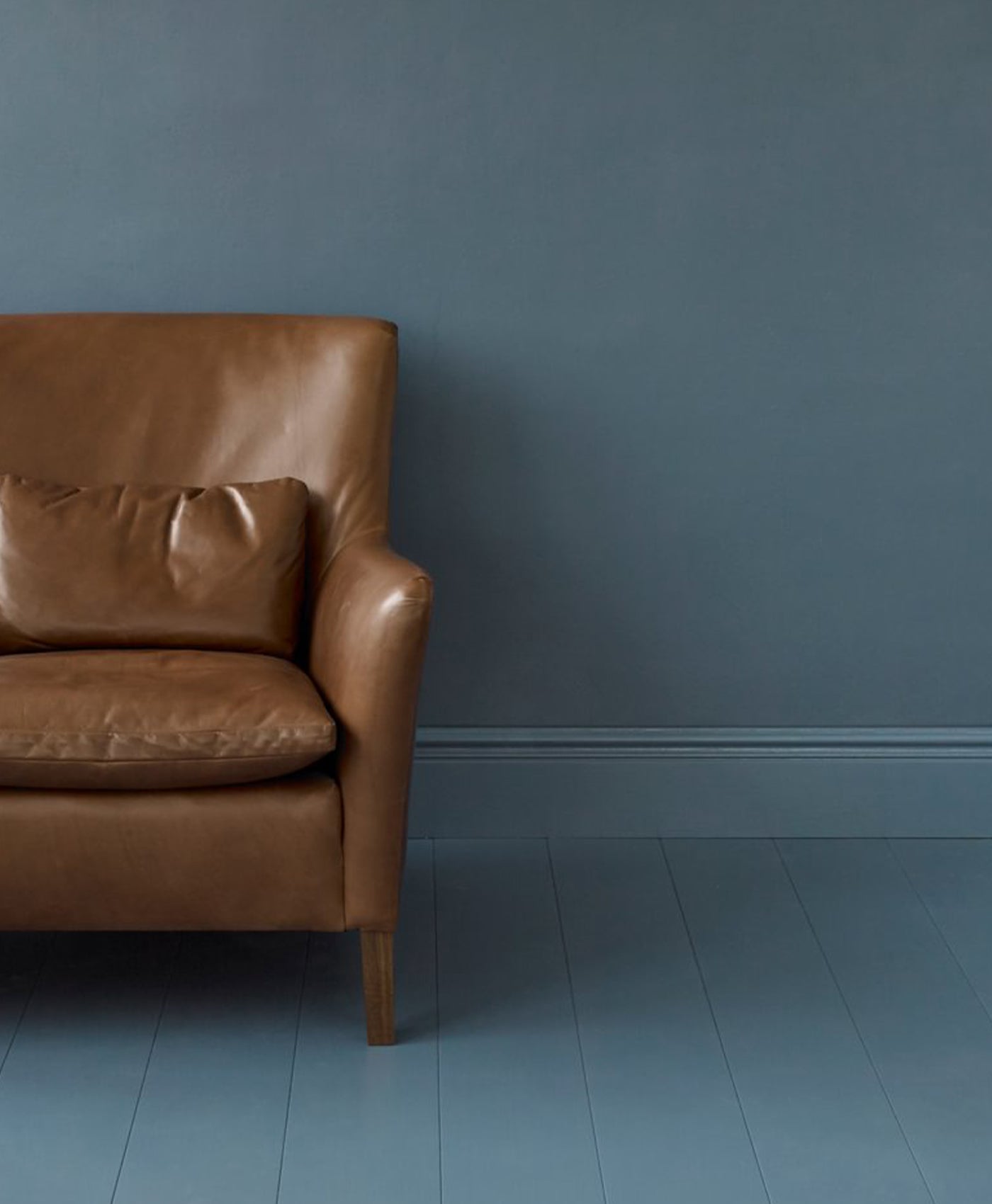 Brown leather armchair against a marine blue wall
