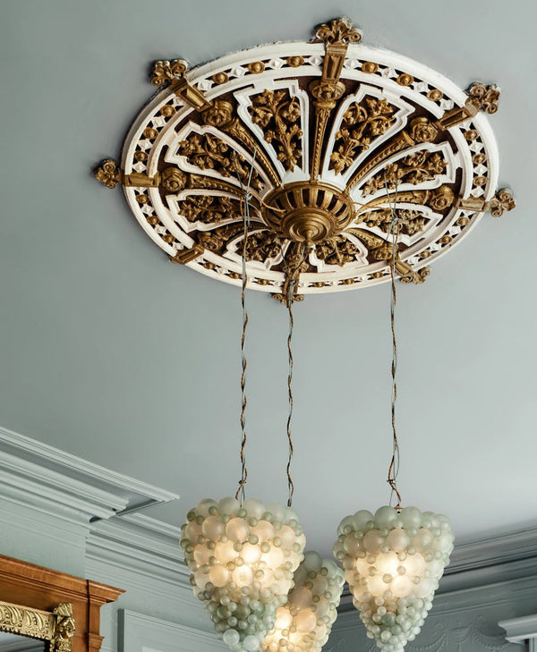 Decorative ceiling rose painted in metallic gold paint with intricate detailing and hanging light fixtures.