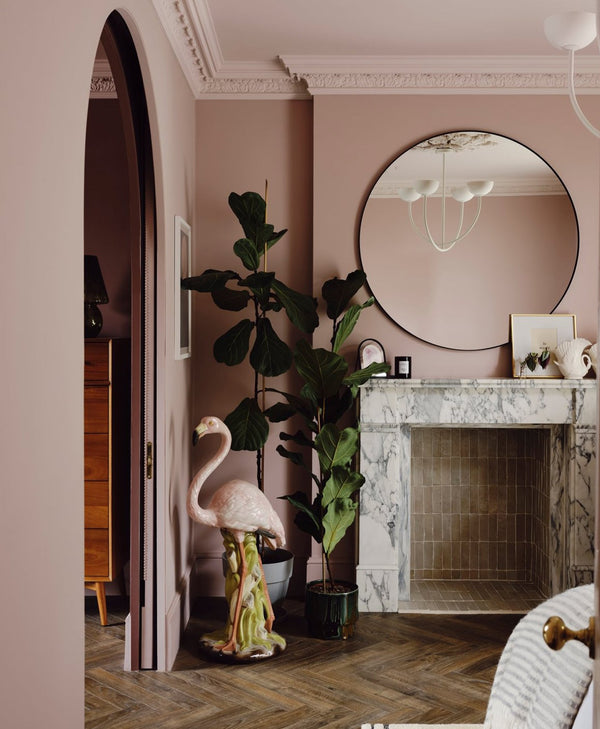 Decorative flamingo statue in a room with plaster pink walls, a round mirror, and a fireplace.