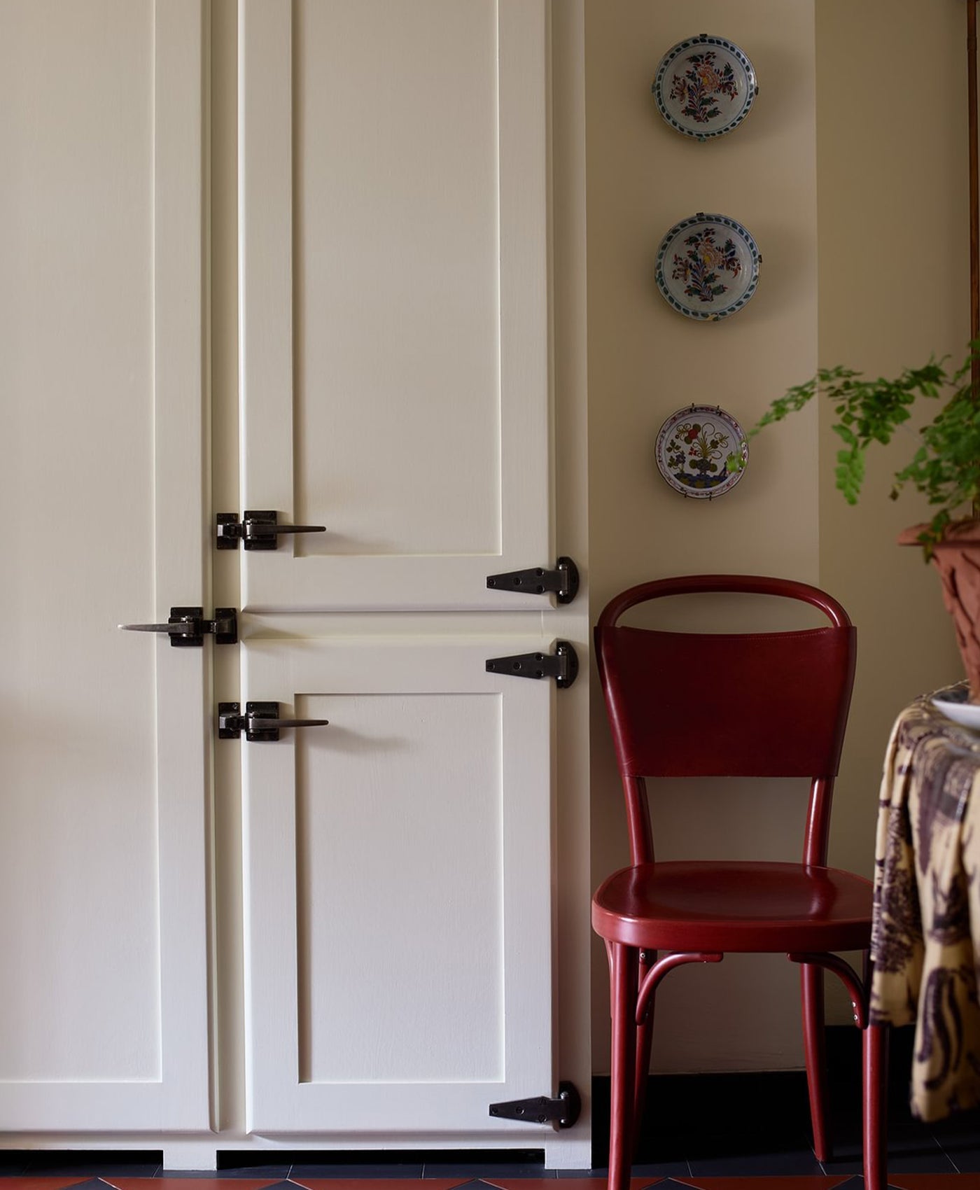 Off-white cabinet with black handles and a red chair against a wall with decorative plates.