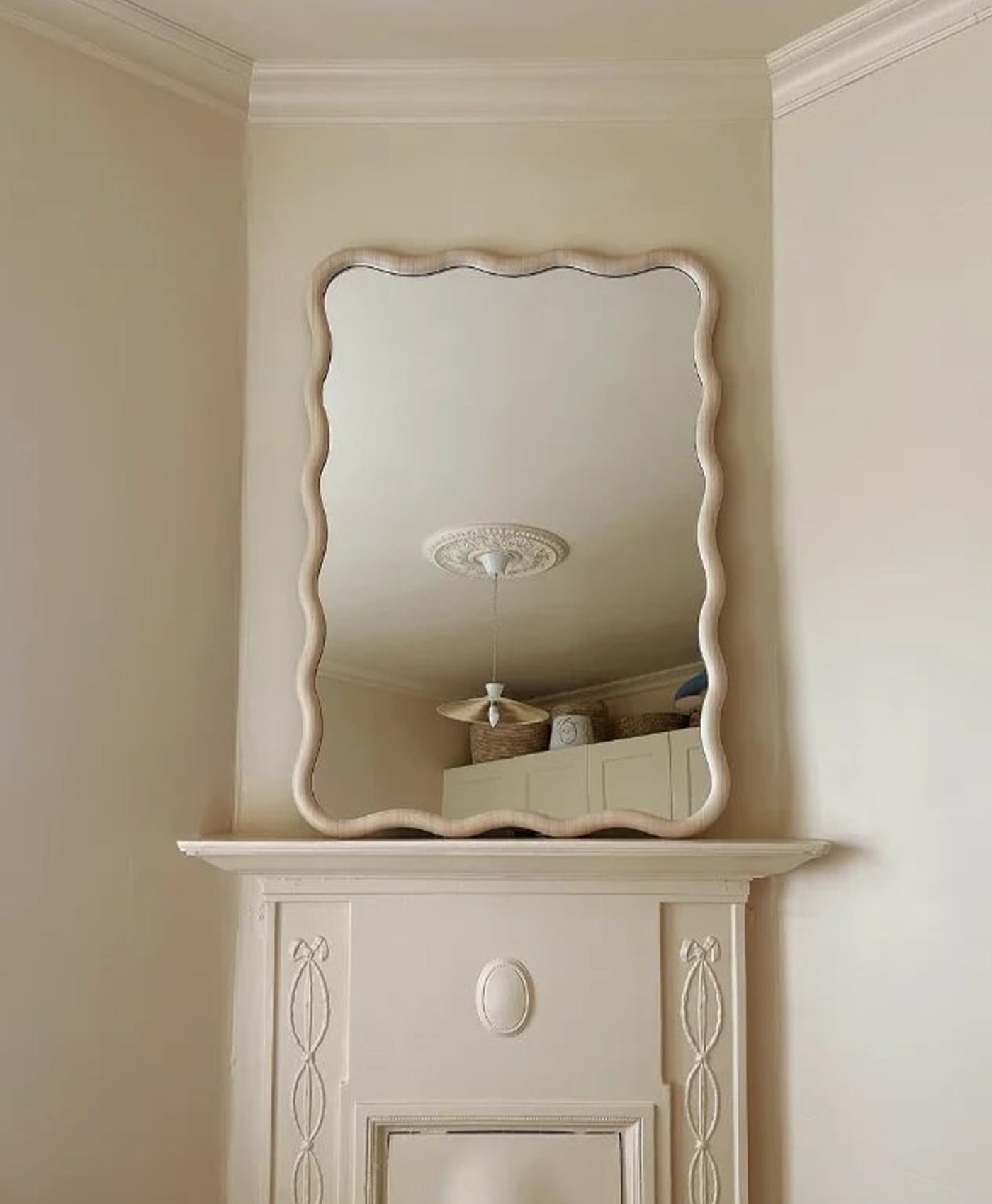Decorative mirror on a wall above a fireplace mantle, painted in cream