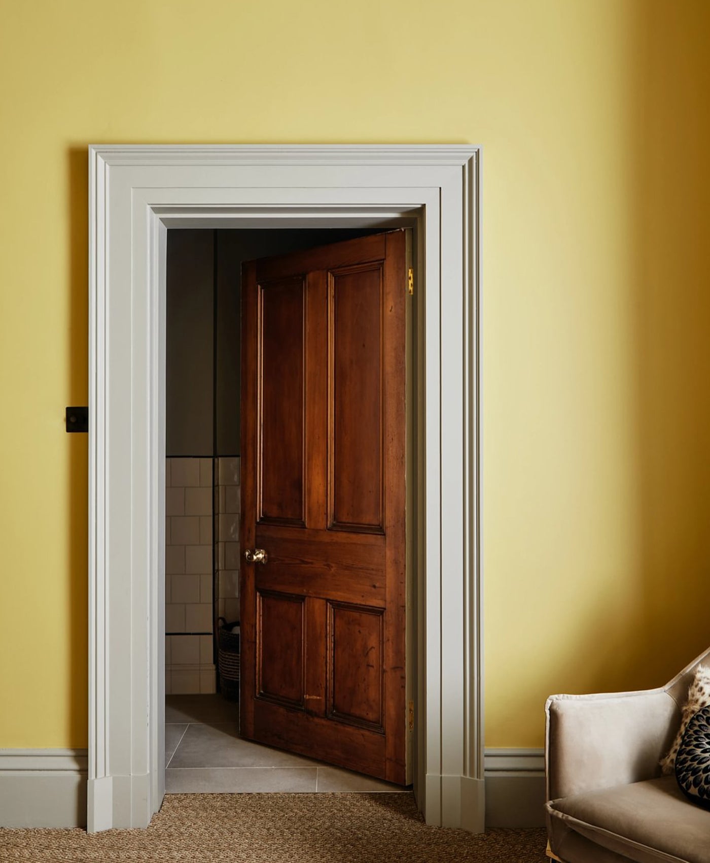 Wooden door in a room with mustard yellow walls and a beige sofa.