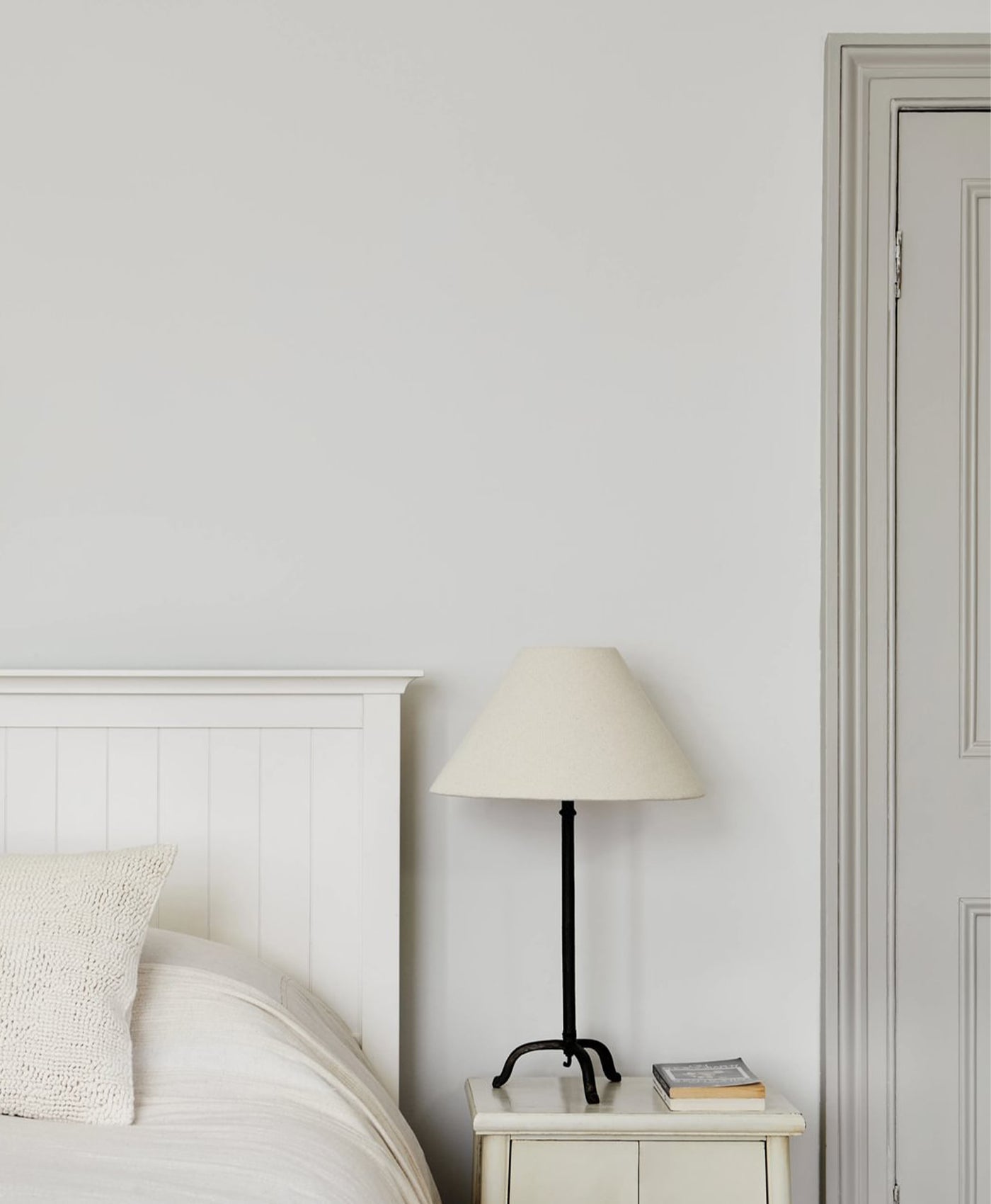 Bedroom with a bed, nightstand, and lamp against a white wall, with grey neutral door frame