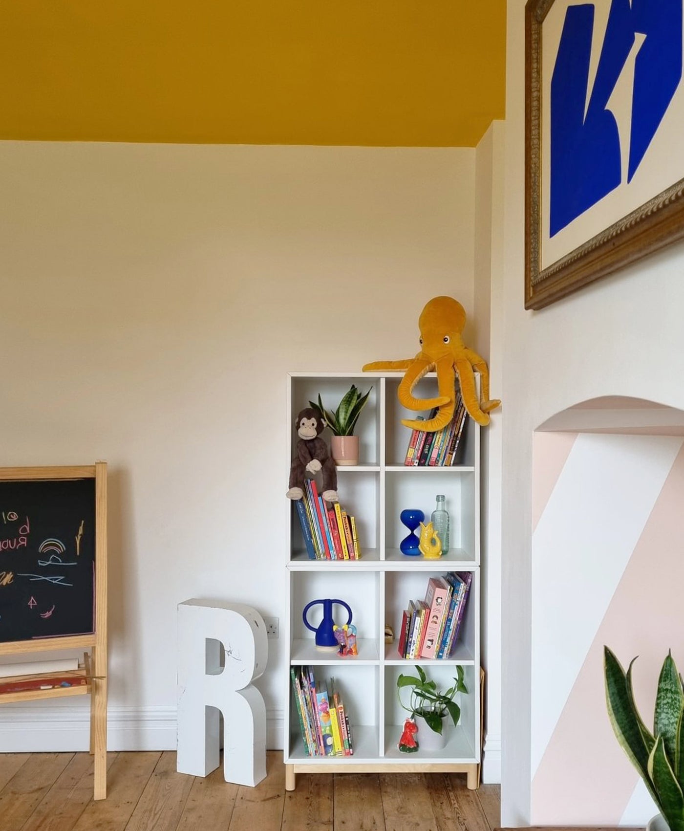 Children's room with a bookshelf, toys, and decorative letters on a yellow wall.