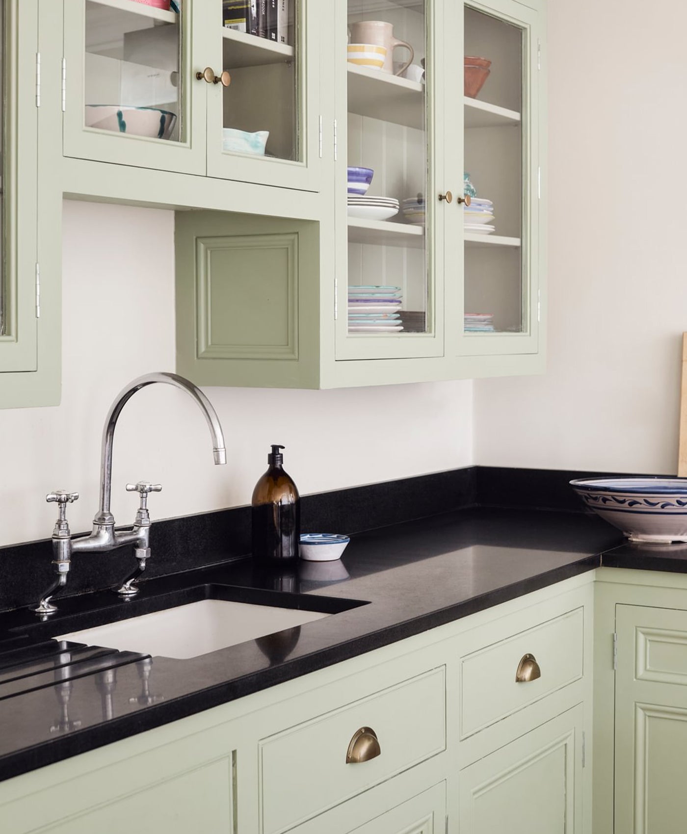 Kitchen with green cabinets, black countertops, and a white sink.