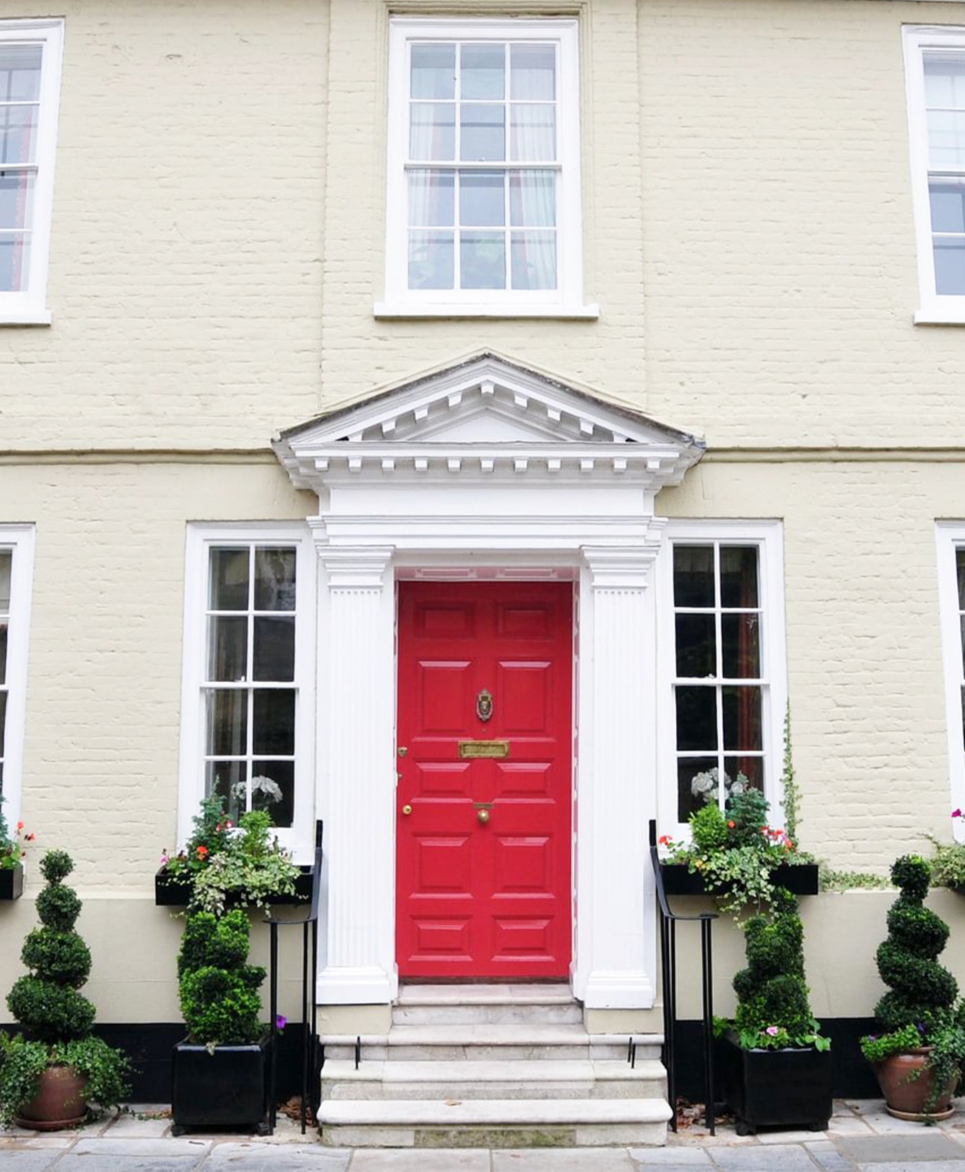 Red door with traditional white paint surround, on a light-coloured building with decorative elements