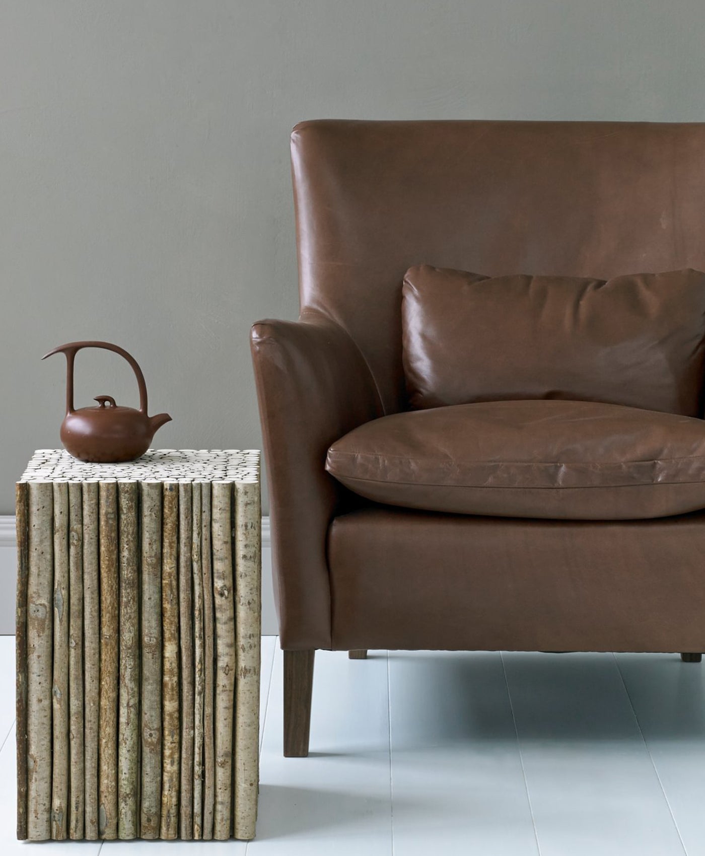 Brown leather armchair next to a textured side table with a teapot on a light grey walls
