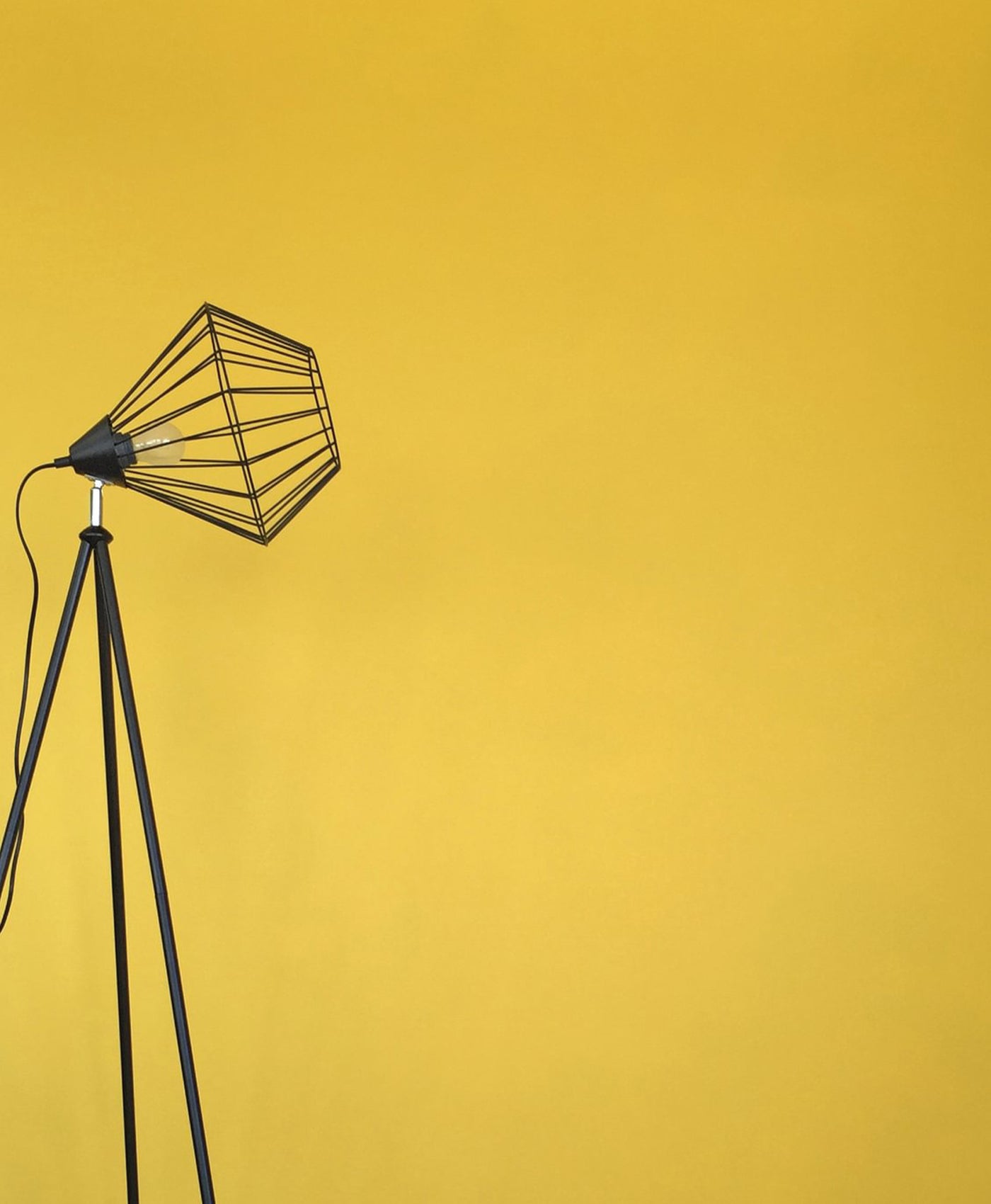 Black floor lamp with wire cage shade on a yellow background