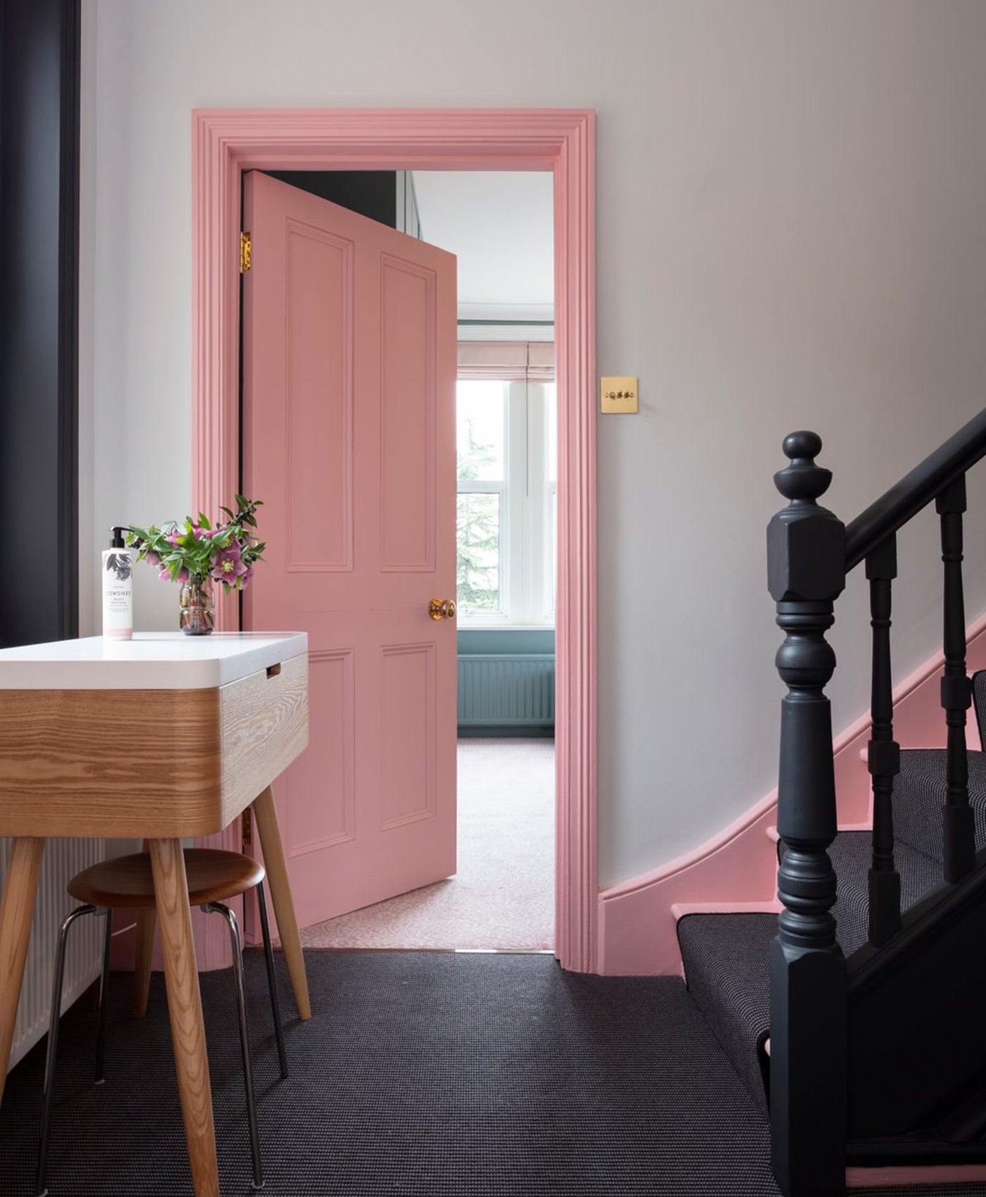 Barbie pink door and skirting in hallway with black banister and window frame.