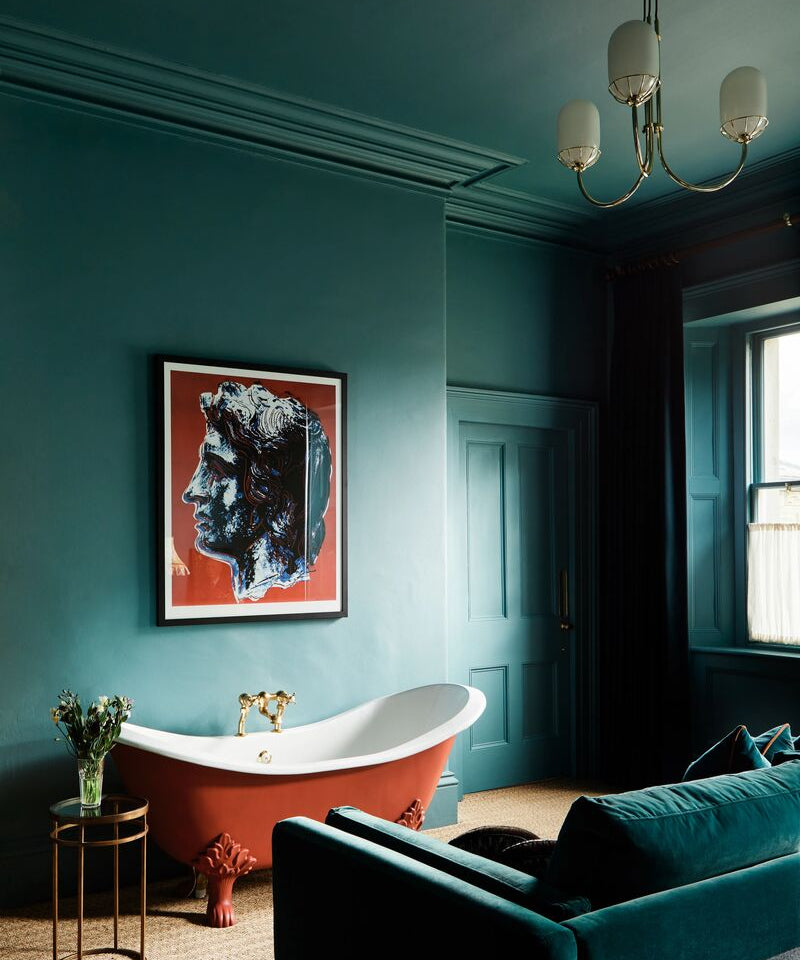 Luxurious bathroom colour drenched with teal paint, freestanding bathtub, and teal sofa.