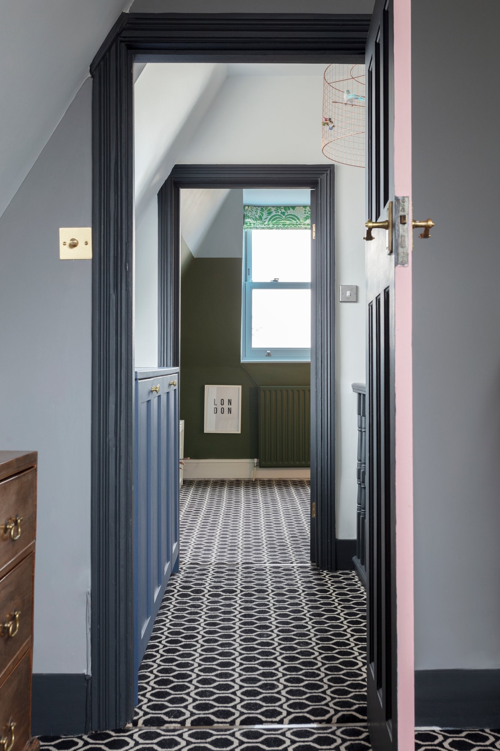 Passage from a room with grey walls black skirting, wooden furniture to another room with a patterned floor.